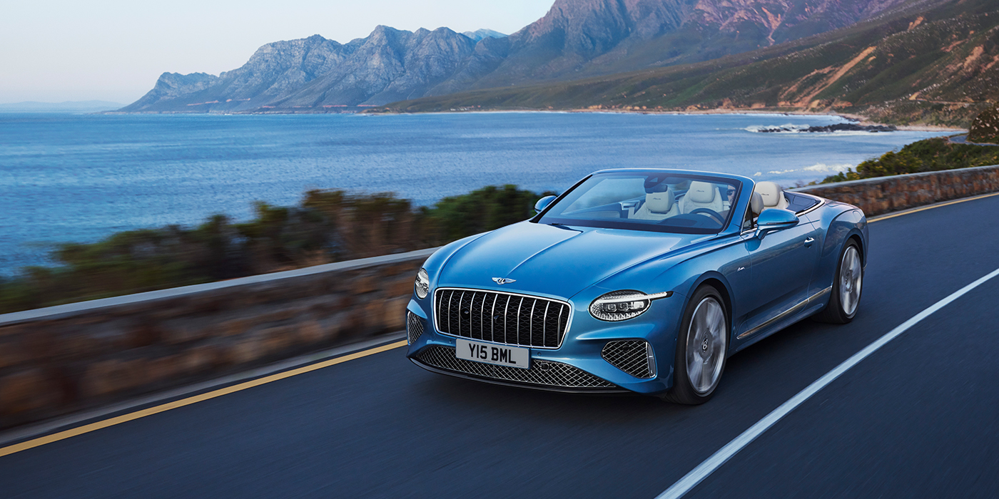 Bentley Luxembourg New Bentley Continental GTC Azure convertible in Light Windsor blue paint with 22 inch Azure wheels and chrome grill, driving dynamically by the sea