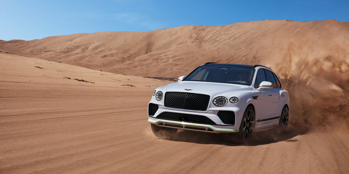 Bentley Luxembourg Bentley Bentayga Speed SUV front three quarter in Snow Quarts Pearlescent by Mulliner white paint driving dynamically through the desert