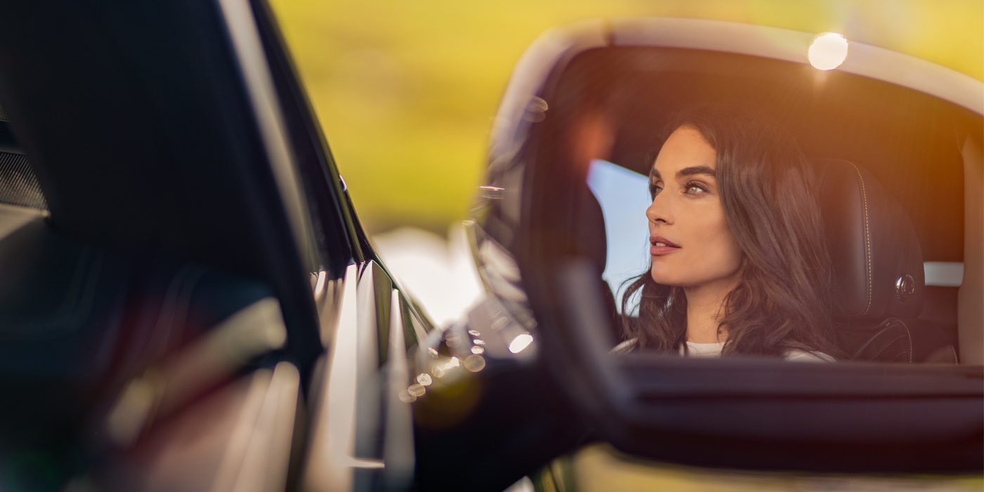 Bentley Luxembourg profile of dark haired woman's face in mirror of Bentley car in sunlight