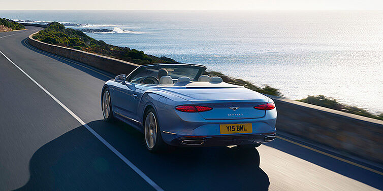 Bentley Luxembourg New Bentley Continental GTC Azure convertible rear view in Light Windsor blue paint with 22 inch ten spoke wheels driving dynamically on an ocean road in the sunshine