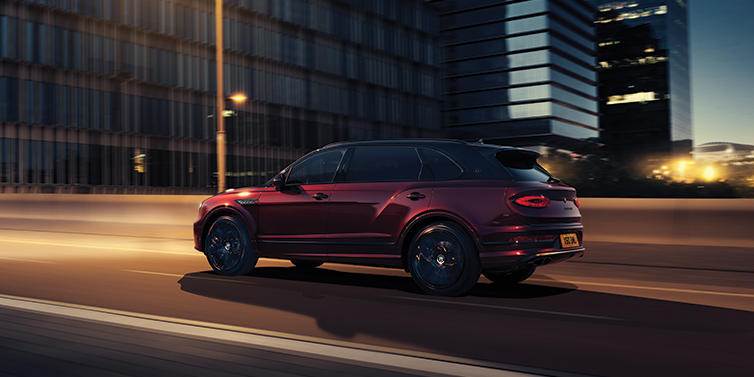 Bentley Luxembourg Bentley Bentayga Extended Wheelbase Mulliner SUV in Cricket Ball red paint driving dynamically in city at night